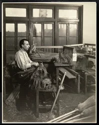 Blind man fastening straw on broom handles at the Bourne Memorial Building, New York, 1921